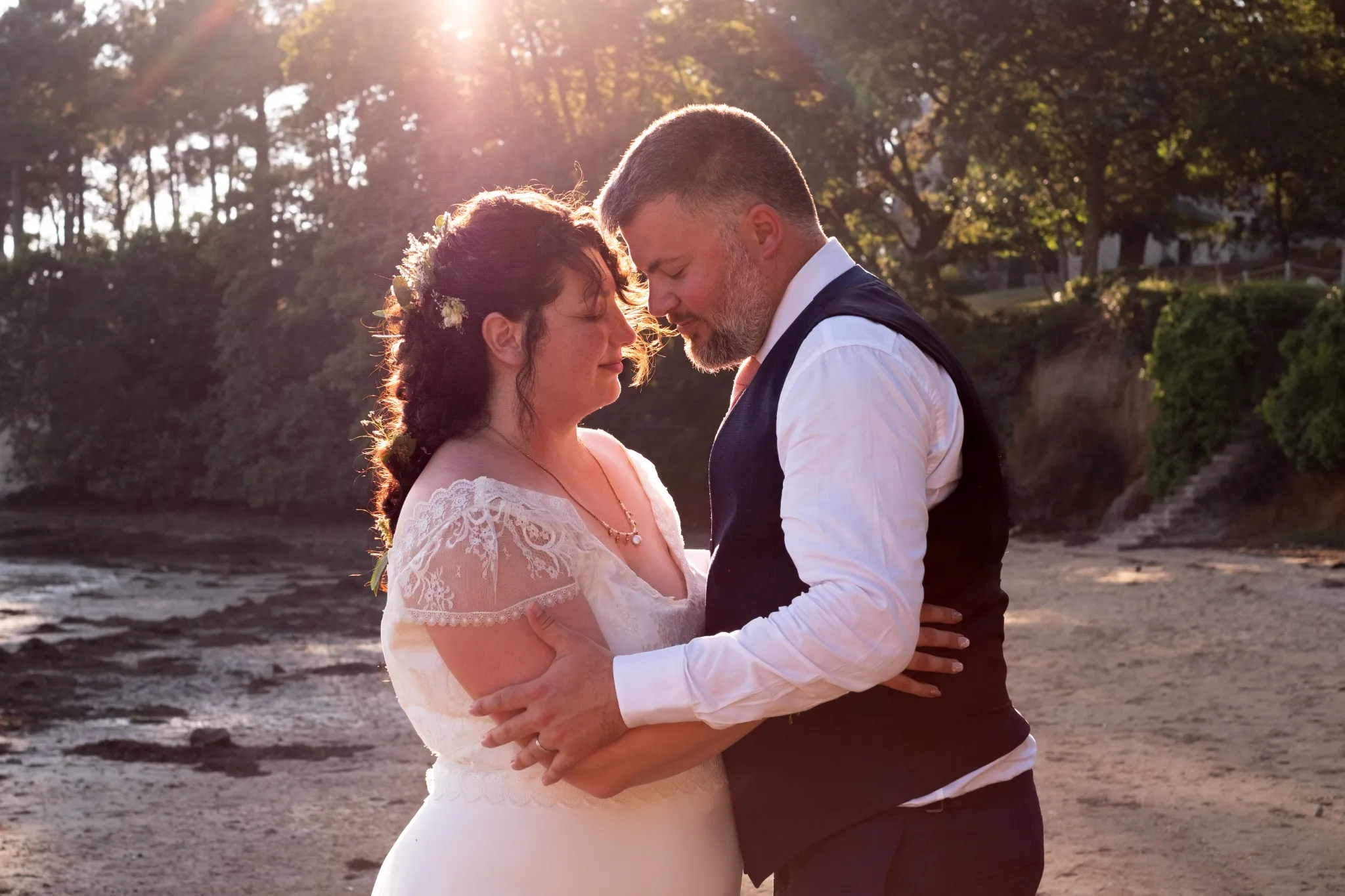 Mariés s’enlaçant sur une plage au coucher du soleil – Photo par Amandine Donato, photographe de mariage à Josselin, Morbihan.
