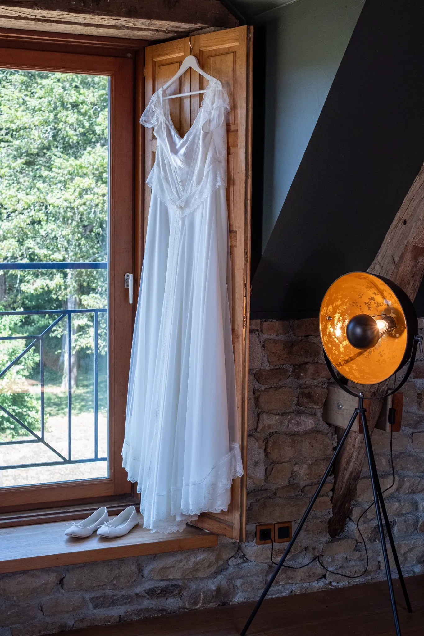 Robe de mariée suspendue avec ses chaussures pendant les préparatifs, photo capturée par Amandine Donato, photographe de mariage à Josselin dans le Morbihan
