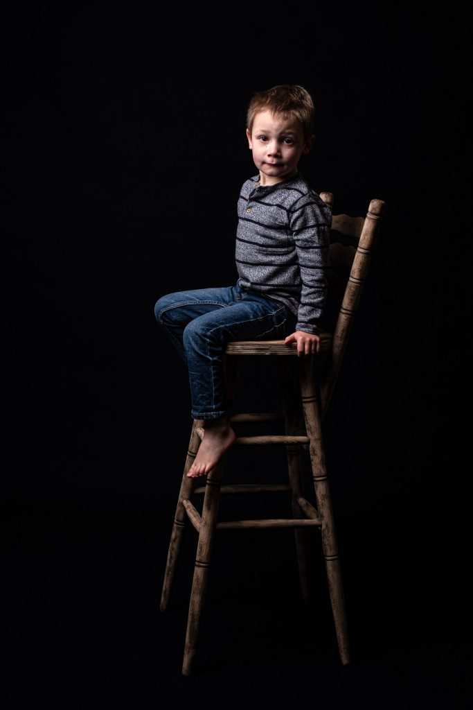 Photographie d’un jeune garçon assis sur une grande chaise en bois, dans un studio photo à Josselin. Une image réalisée par Amandine Donato, photographe.